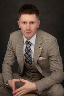 Mężczyzna w stylowym garniturze w kratę i krawacie, siedzący na tle ciemnym, portret biznesowy wykonany w studio w Krakowie