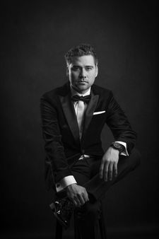 Czarno-biały portret eleganckiego mężczyzny w smokingu siedzącego na stołku – męska sesja zdjęciowa Kraków