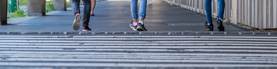 A close-up of a crosswalk with the feet/lower legs of three people walking away.