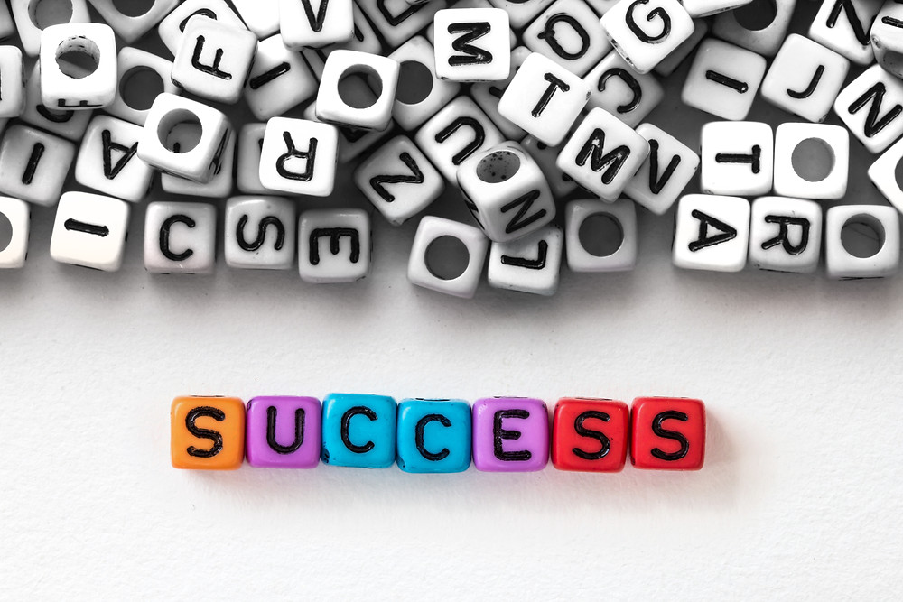 The word success is spelled out in color in front of a pile of black and white letters.