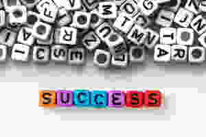 Das Wort "success" wird in Farbe vor einem Stapel schwarzweißer Buchstaben dargestellt.
