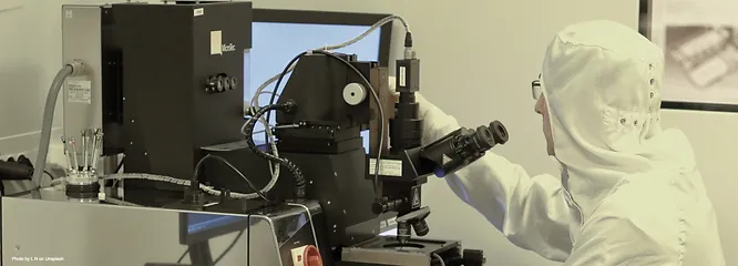 a scientist in a full protective suit working in front of a digital microscope 