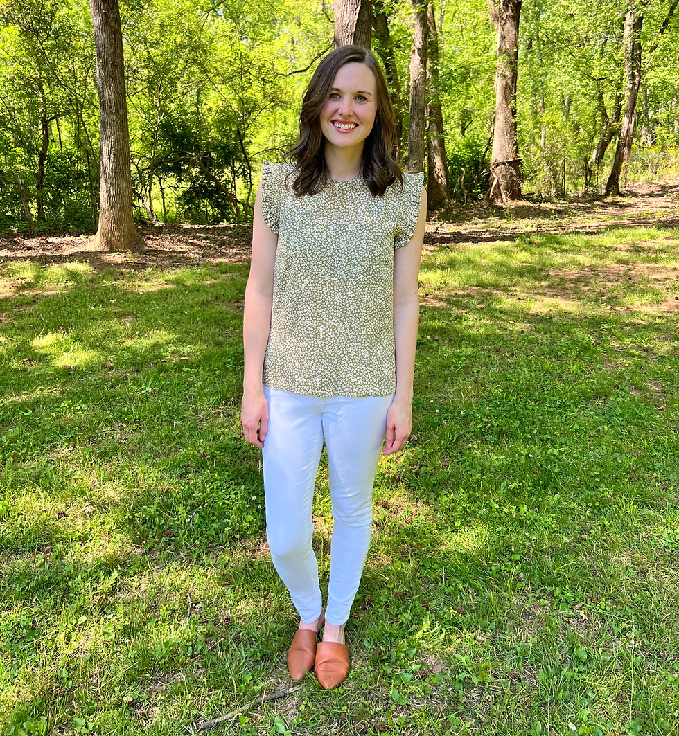 Full-body picture of occupational therapist. She has brown, short hair and is wearing a flowered shirt with white pants.