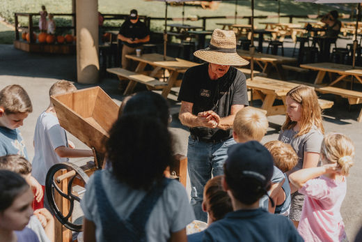 Man shows children antique grain mill