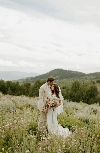 Wedding couple embracing in a field of wildflowers with mountains