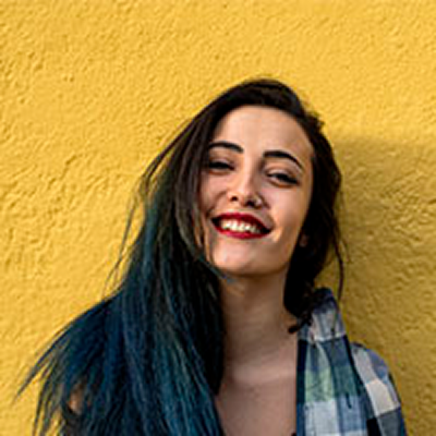 Smiling woman with teal hair against yellow wall