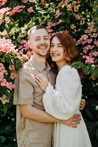 Smiling couple embracing in front of pink flowers