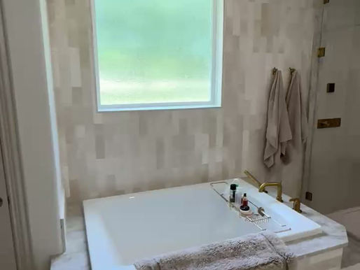 This image features a steam shower with floor-to-ceiling frameless glass and gold fixtures. Two towels are hanging to the left of the glass enclosure and two bottles sit on a shelving niche. This picture is taken at a home in Prosper Texas. #steamshower #showerdesign #goldfixtures #homedesign #luxuryrealestate #prosper #prospertexas