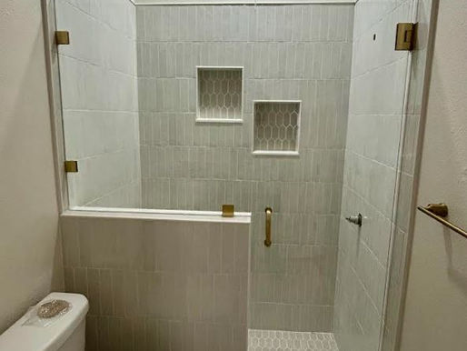 This image captures a bright, neutral bathroom with a half-wall glass partition and Satin Brass hinges.