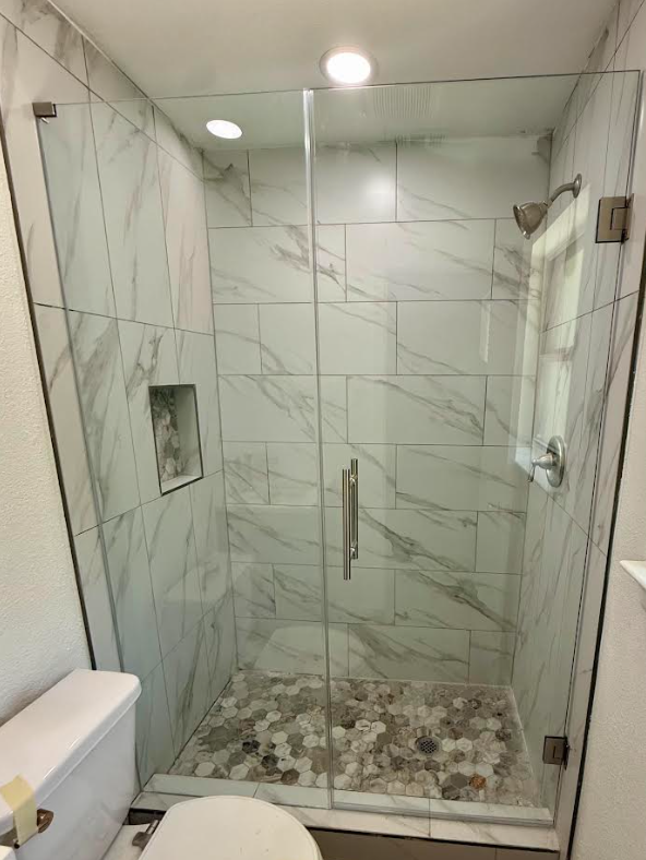 A custom frameless shower enclosure showing a unique glass-on-glass corner installation on a half-wall in an Irving home.