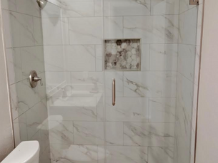 Two-panel frameless glass shower enclosure with brushed nickel hinges and marble-style tile in Irving, Texas