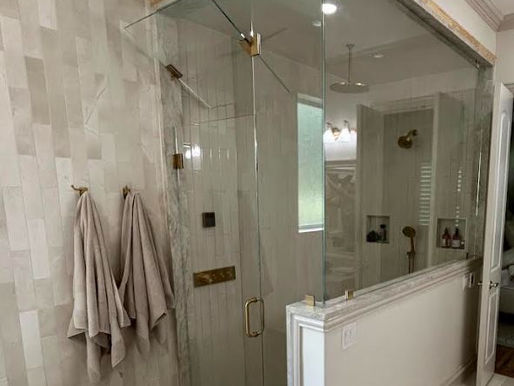 Custom floor-to-ceiling glass steam shower enclosure featuring premium brushed bronze hardware hinges, and a closed movable glass transom positioned above the door.