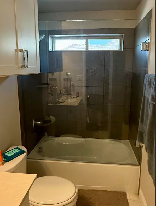 Clean guest bathroom bathtub alcove featured with a clear frameless glass shield and chrome fittings in McKinney, Texas.