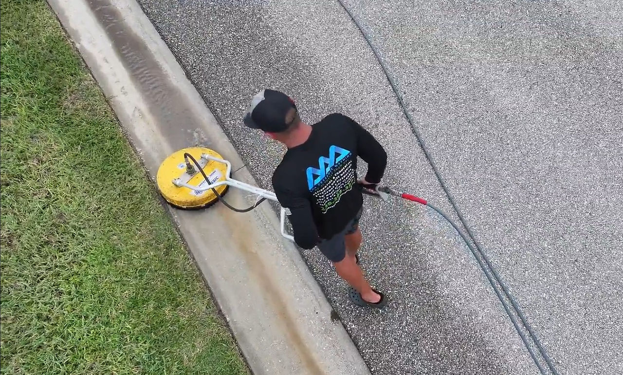 Close-up of Dan using a pressure washing surface cleaner on neighborhood gutters, lifting dirt and algae for a fresh, revitalized look.
