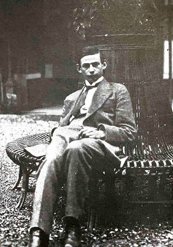A young Gerhard Scholem in a suit sits nonchalantly on a park bench, one hand in his pocket, the other on his lap