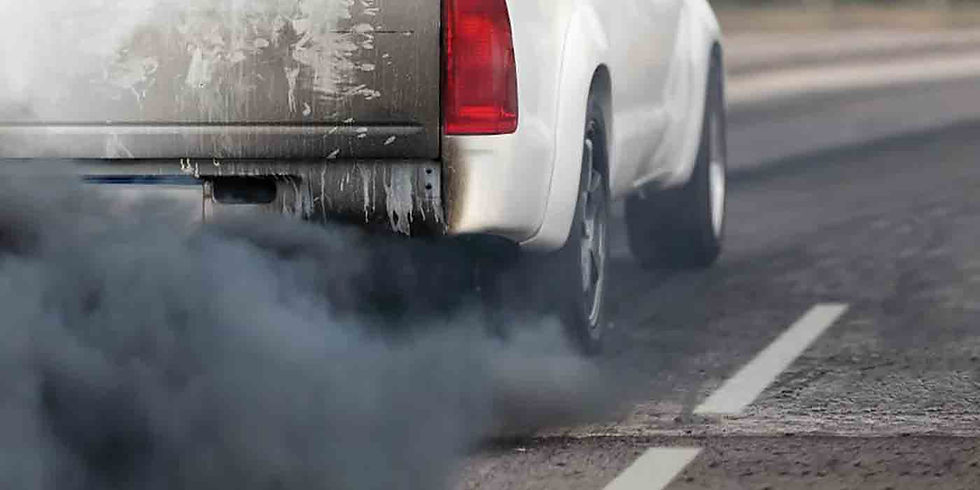 A white truck emits thick black smoke from its exhaust on a road. The tailgate is dirty and worn, contrasting with the clean roadway.