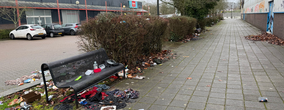 a lot of litter and debris around a bench outside a building with graffitti
