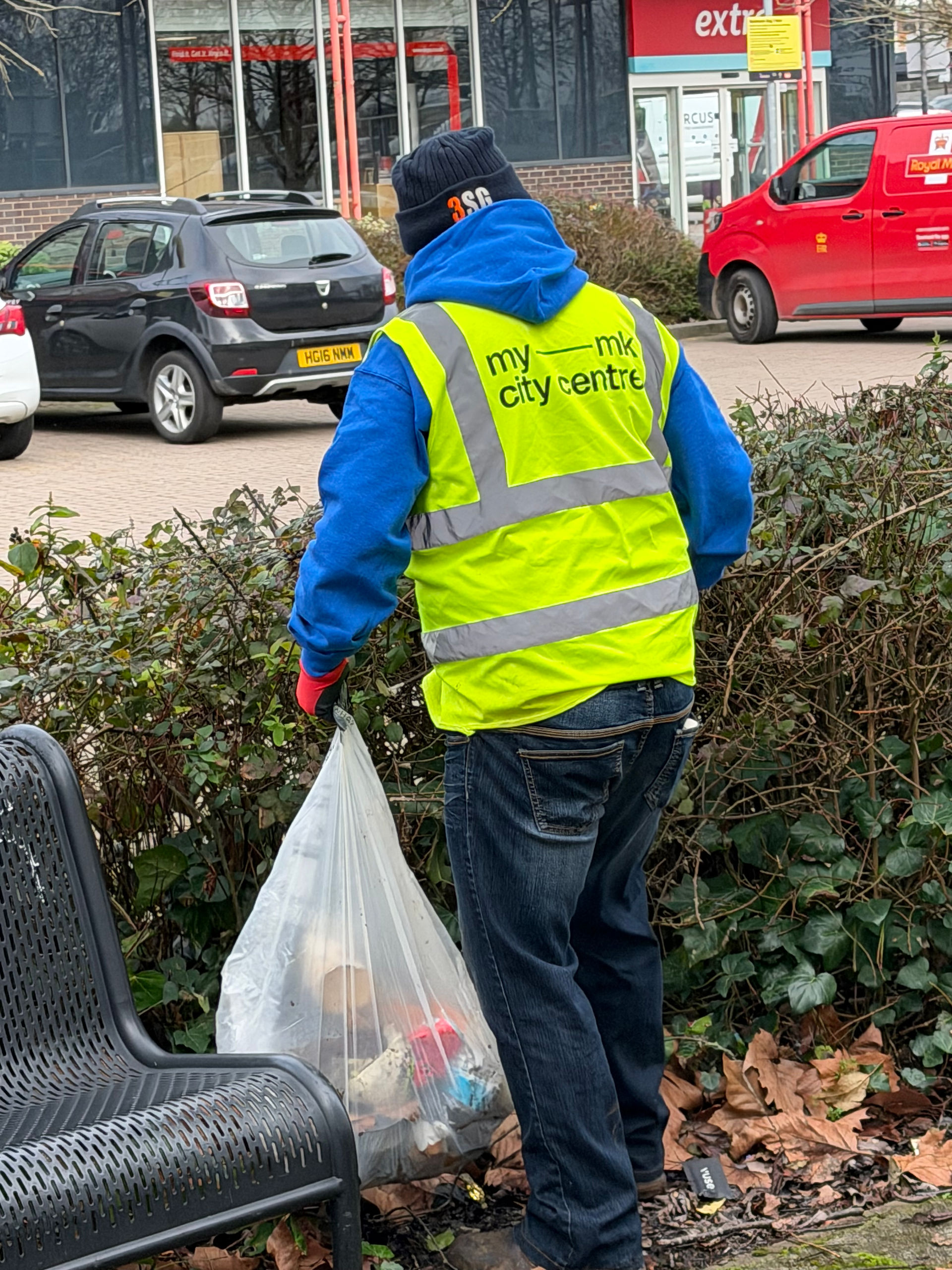 A person in a blue hoody and yellow high vis collecting litter