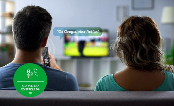 Um casal está sentado em um sofá assistindo TV. O homem segura um controle remoto e um balão de fala diz: "Ok Google, abra a Netflix." Um círculo verde no canto inferior esquerdo exibe um ícone de comando de voz com texto em português promovendo o controle de voz.