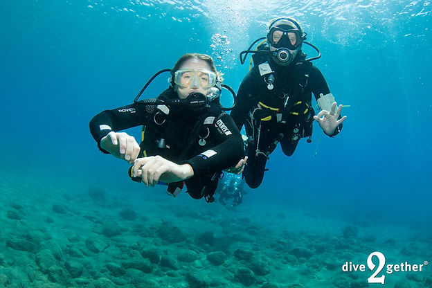 A female scuba diving instructor guides a girl on a PADI introduction dive in calm shallow water off the south coast of Crete