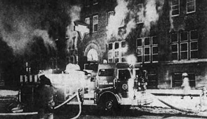 Historic black and white photo showing a fire truck in front of a brick building with smoke pouring from the windows during the Rock Island fire.