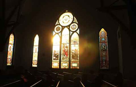 Detailed view of the historic stained glass windows inside Father John's Church in Bryan, Ohio, with natural light filtering through.