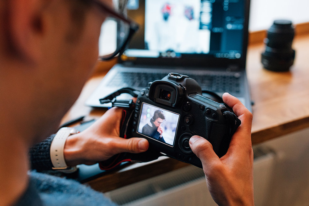 male-hands-holding-professional-camera-looks-photos-sitting-cafe-with-laptop copie.jpg
