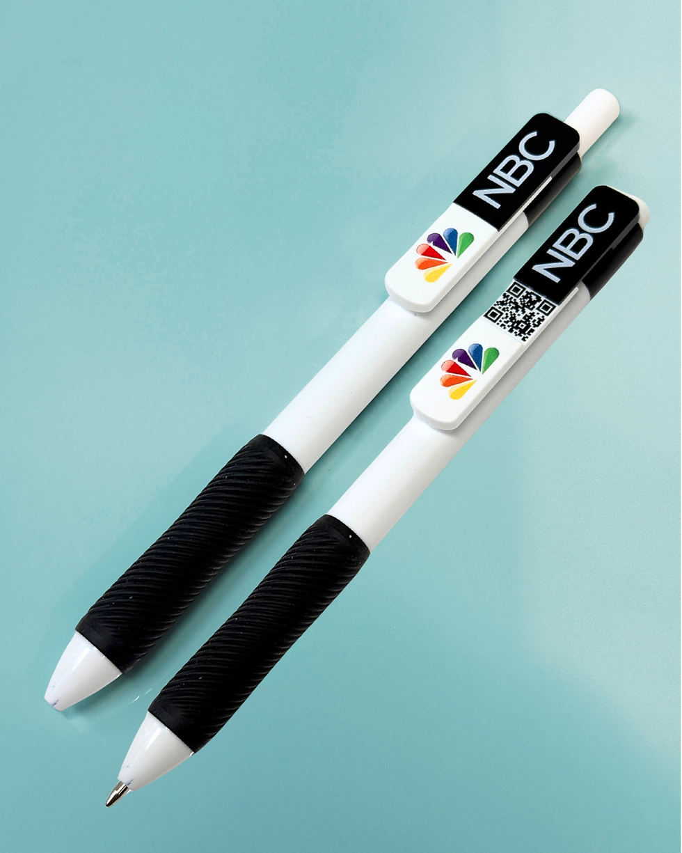 Two white pens with black grips on a light blue surface. Clips show NBC logo and a QR code. Bright and clean appearance.