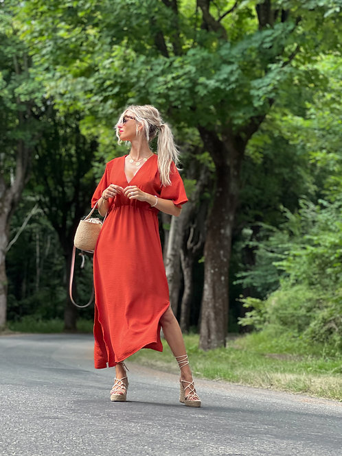 Robe longue rouge sombre. Les manches sont courtes. Le décolleté est en V et la taille marquée.