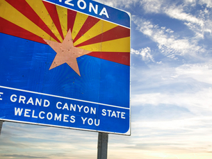 Image of a road sign with the Arizona flag reading "The Grand Canyon State Welcomes You"