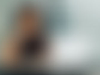 Gen X woman thinking with hand on chin, sitting at a desk with a laptop and notebook. Glass partition background, neutral colors, focused mood.