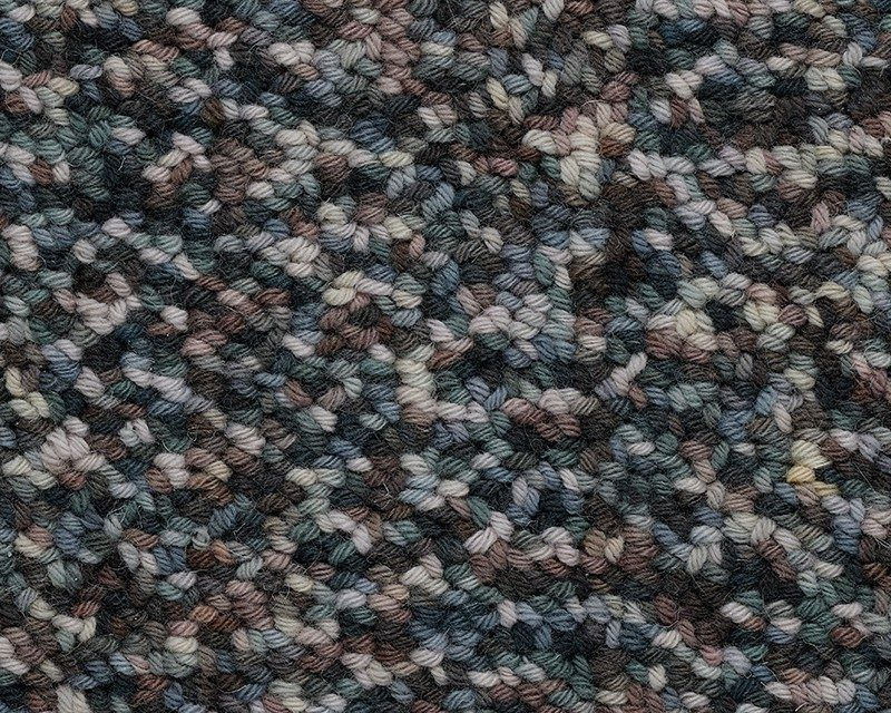 Close-up of a carpet sample with a mottled pattern of grey, blue, and brown fibers.