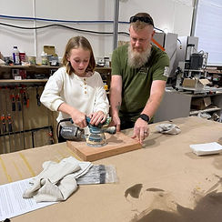 Girl sanding wood with an adult in a workshop
