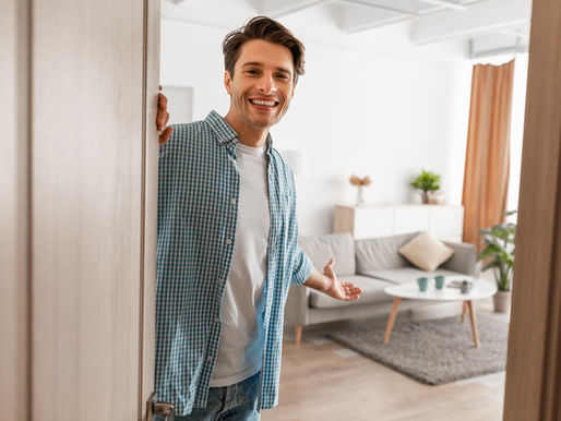 Man holding open a door to a home with a welcoming gesture.