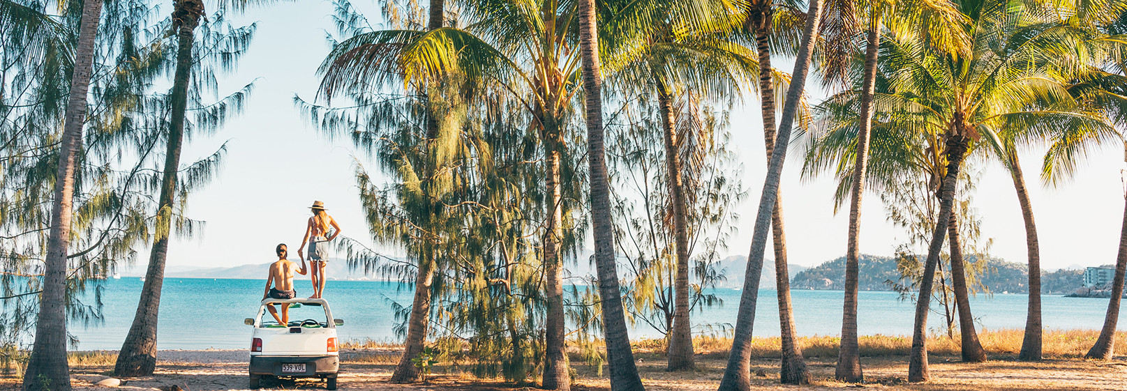 Couple sitting on car overlooking Magnetic Island beach with palm trees