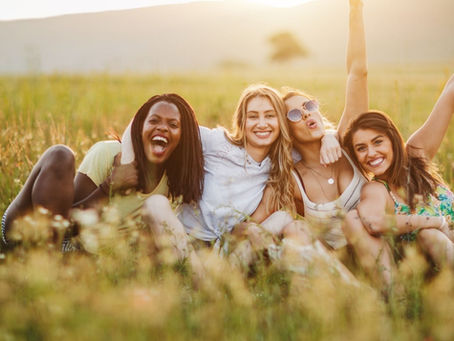 Selbstbewusstsein stärken bei Jugendlichen: Vier junge Frauen sitzen lachend auf einer Wiese in der Abendsonne – ein Symbol für Zugehörigkeit, Freundschaft und stärkende soziale Verbindungen in der Jugend.