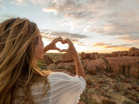 Selbstliebe lernen: Frau blickt in eine weite Landschaft und formt mit den Händen ein Herz vor dem Himmel als Symbol für Selbstannahme, innere Weite und Verbundenheit mit sich selbst.
