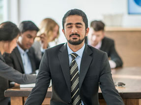 Work Life Balance Maßnahmen – Businessmann meditiert im Büro mit geschlossenen Augen als Symbol für Achtsamkeit und Stressreduktion am Arbeitsplatz.