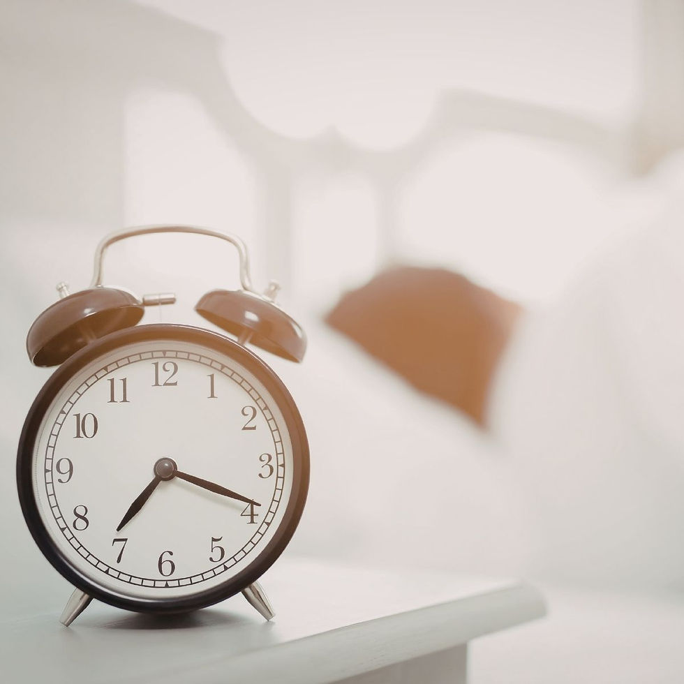 Guter Start in den Tag: Wecker auf einem Nachttisch vor einem hellen Bett als Symbol für bewusstes Aufwachen und eine ruhige Morgenroutine.