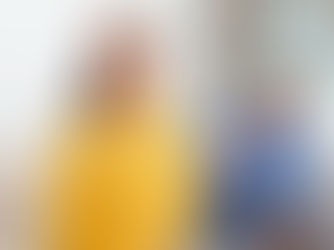 Frau im gelben Pullover hält mit ausgestreckter Hand einen hinter ihr sitzenden Mann auf Abstand.
