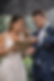 Bride and groom standing in the rain reviewing a wedding timeline with a clipboard while holding an umbrella during an outdoor ceremony setup, showcasing real-time problem solving and professional wedding planning support.