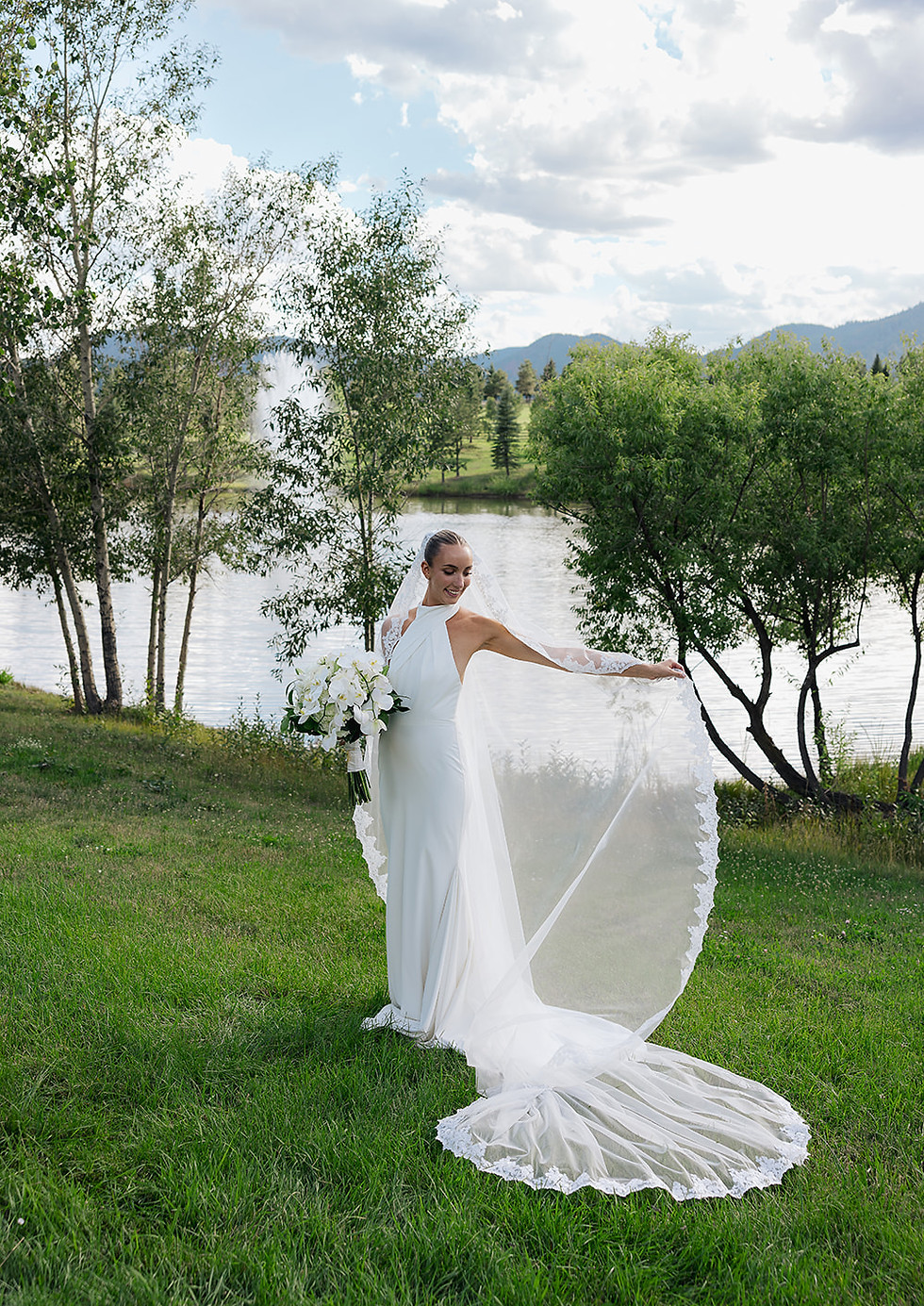 Bride displaying her veil beside the lake at Spruce Mountain Ranch during her Colorado wedding.