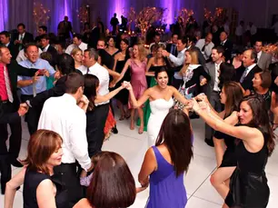 People in formal attire dance joyfully in a circle at a wedding reception.