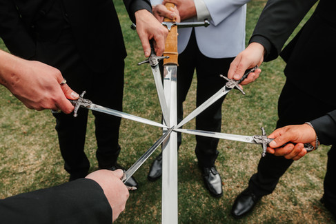 Groomsmen holding ceremonial swords in a circle before the wedding ceremony at The Oaks at Plum Creek in Castle Rock, Colorado.