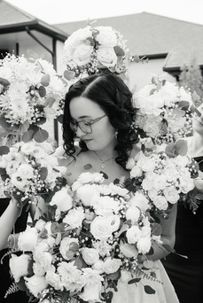 Bride surrounded by white wedding bouquets featuring roses, chrysanthemums, and eucalyptus.