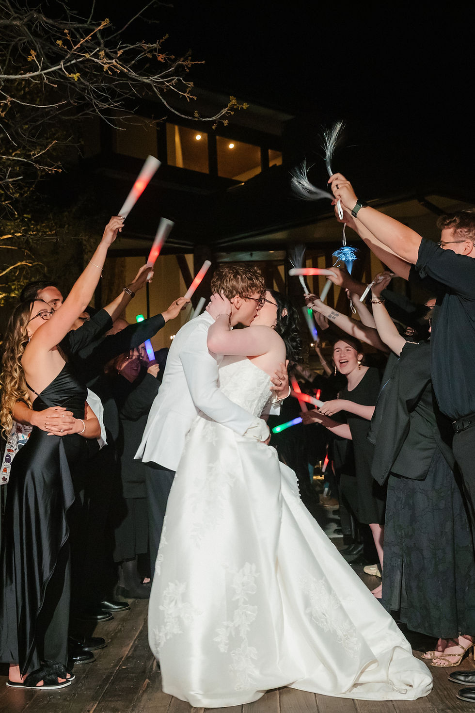 Evelyn and Charles celebrating their wedding exit surrounded by guests holding glowing light sticks at The Oaks at Plum Creek.