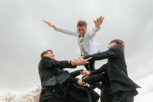 Groom being lifted into the air by his groomsmen during wedding portraits.