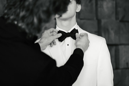Groom adjusting his black bow tie while getting ready in a white tuxedo before his Colorado wedding.