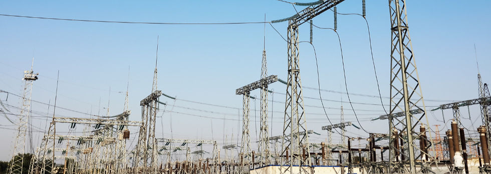 High-voltage electrical substation with transmission towers, power lines, and insulators spread across an outdoor utility facility under a clear blue sky.