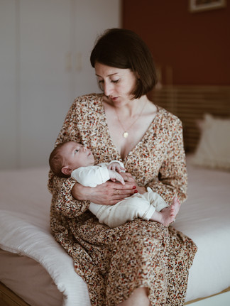 PHOTO d'une mère assise dans son salon sur son canapé qui berce son bébé dans ses bras en le regardant avec tendresse